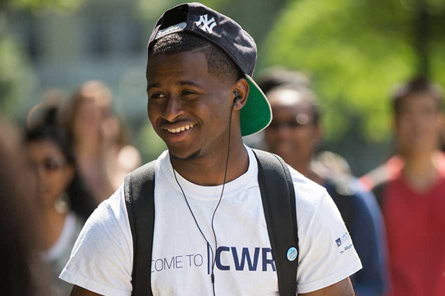 Photo of a Case Western Reserve University student wearing headphones, walking outdoors and smiling